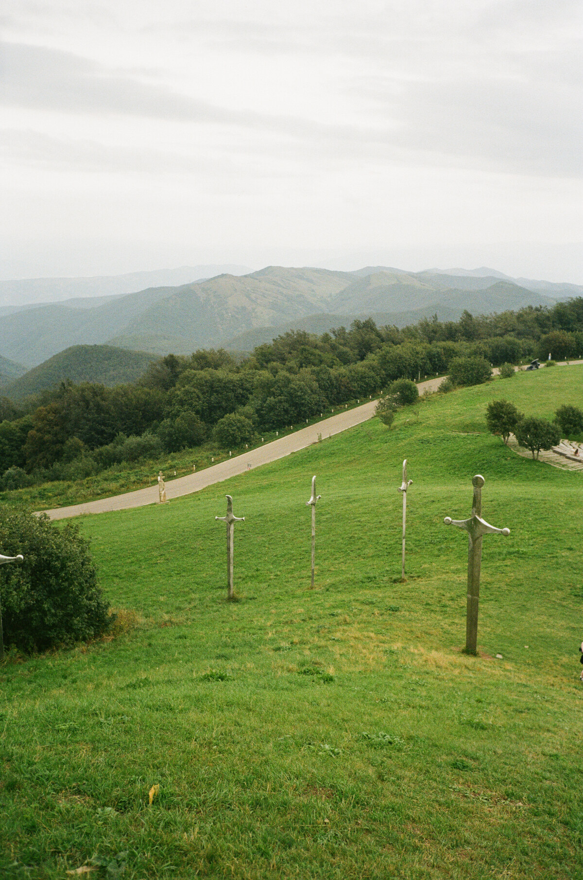 The Didgori Battle Memorial in Georgia, with monumental sword sculptures rising from a green hillside below mountain ridges.