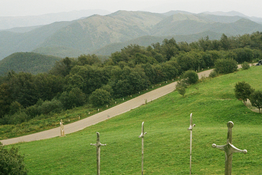 The Didgori Battle Memorial's monumental swords, hillside road, and mountain ridges encoded as JPEG quality 90.